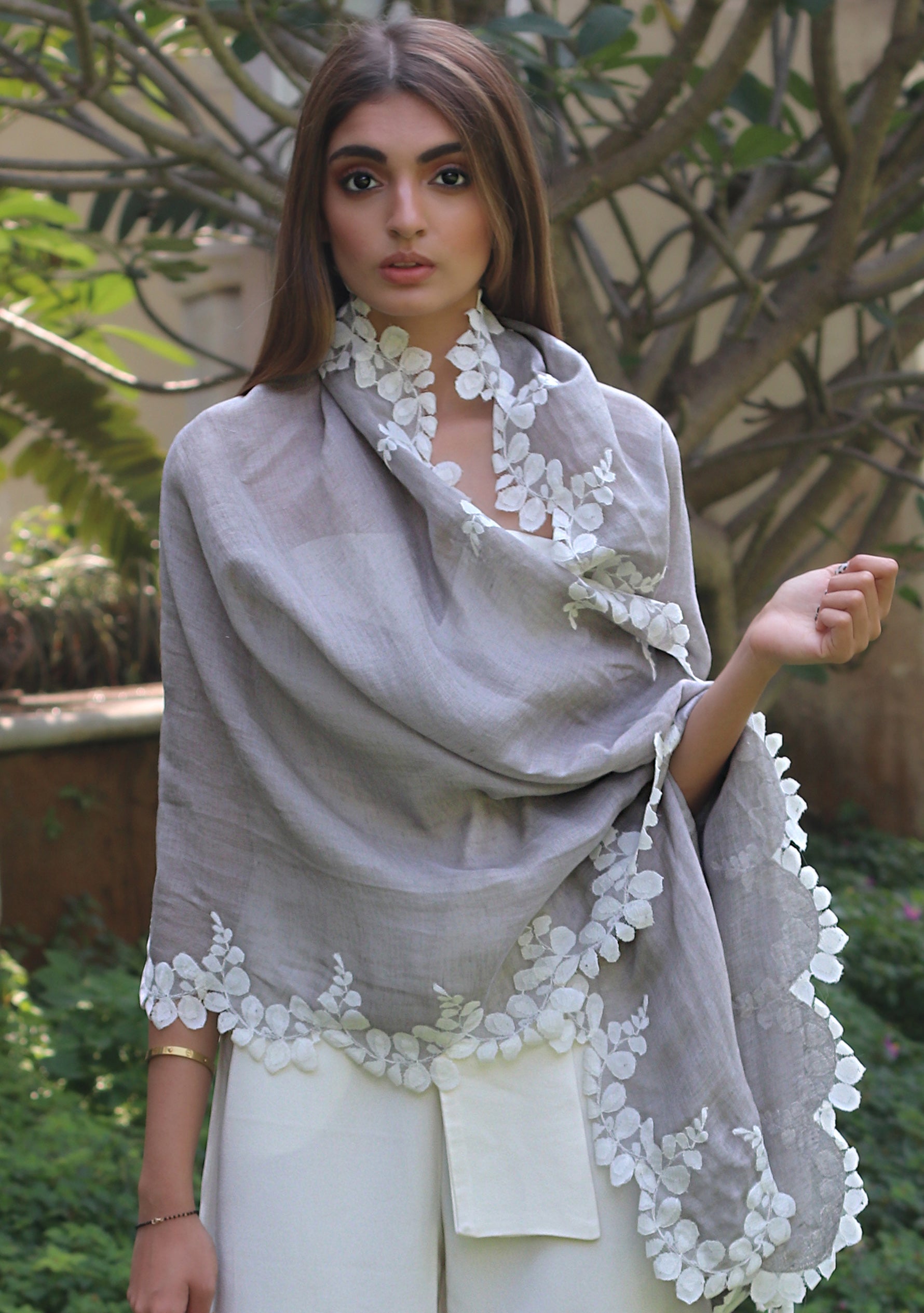 Woman wearing a gray shawl with white lace details in an outdoor setting